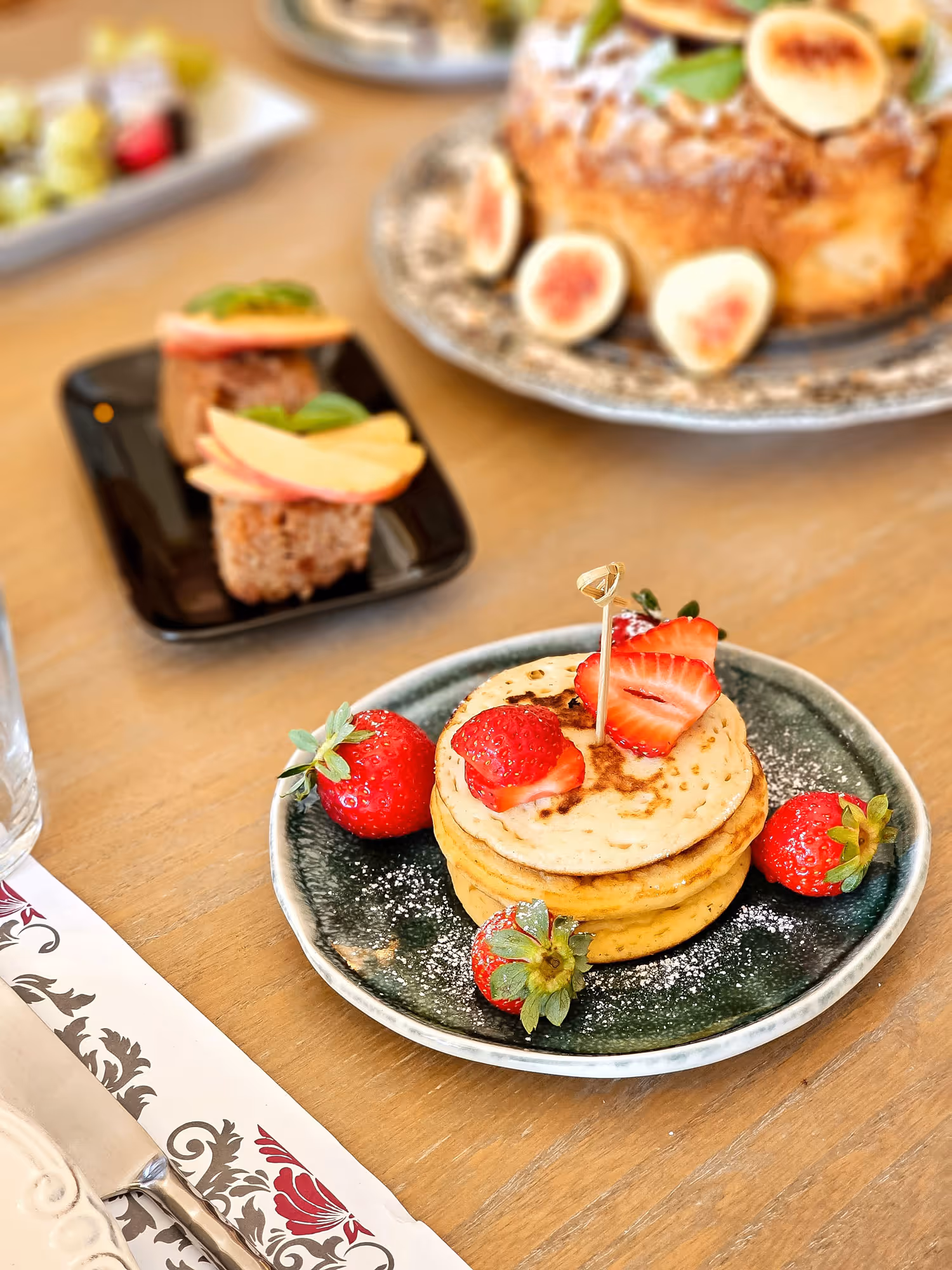 Stack of pancakes topped with sliced strawberries and surrounded by whole strawberries on a plate.