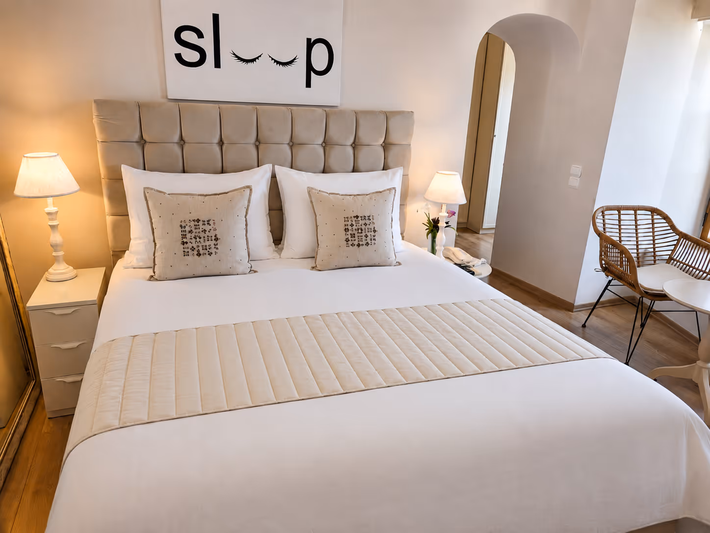 Neatly made bed with beige pillows, a quilted headboard, two bedside lamps, and a sign that reads sleep.