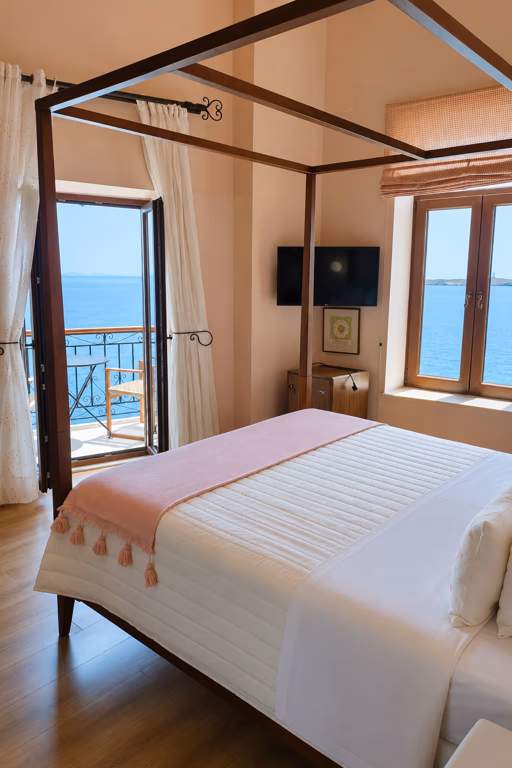Bedroom with a canopy bed, open balcony doors, and windows showing a blue sea view.