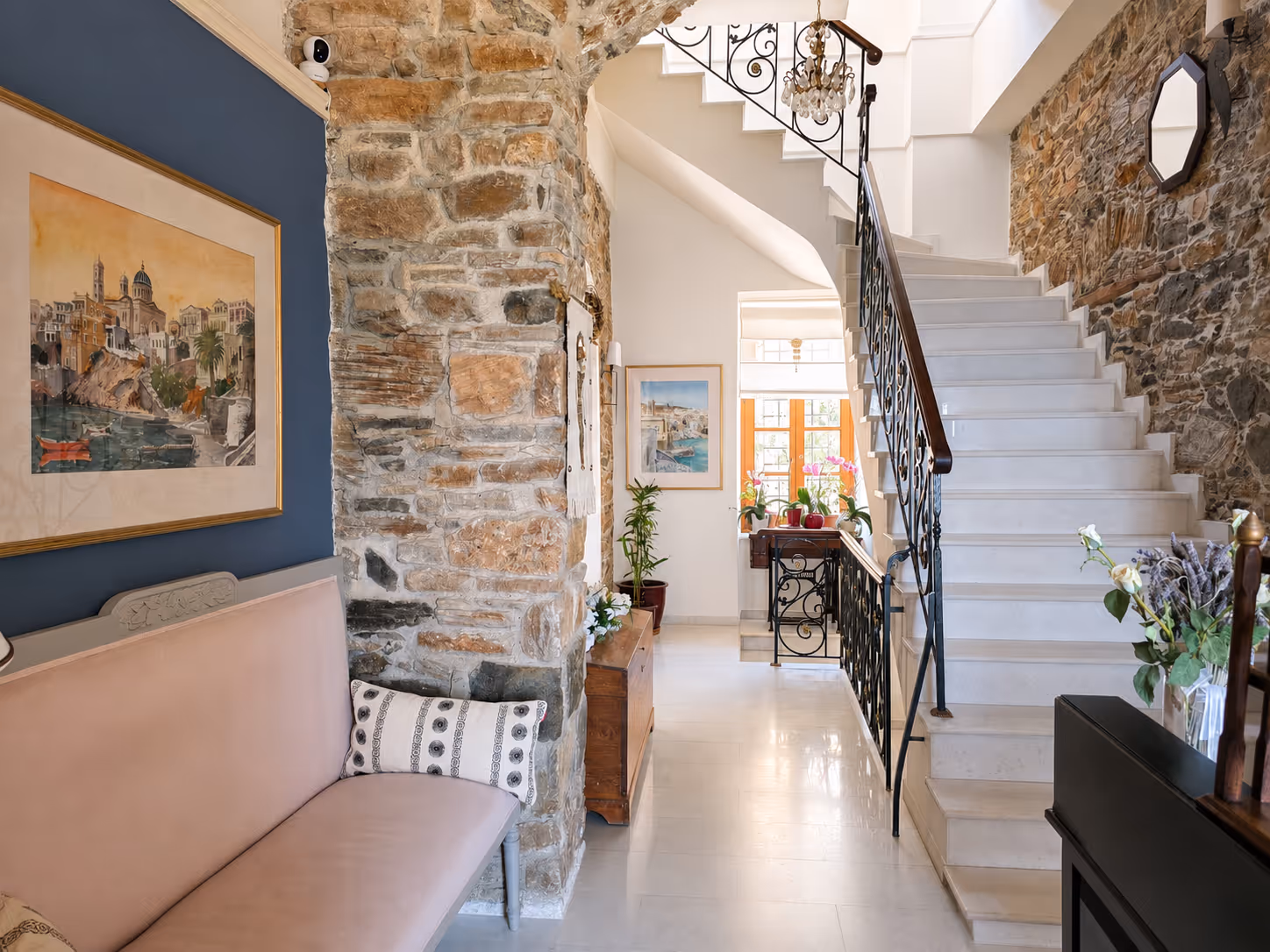 Cozy hallway with stone walls, a bench, white marble stairs, and plants by a sunny window.